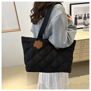 Detail view of a black quilted tote bag featuring a decorative brown floral leather patch