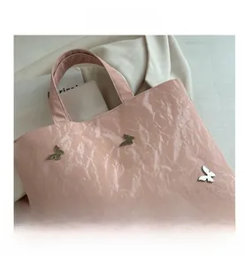 Detail van roze metallic draagtas met plooitextuur en metalen vlinderaccenten