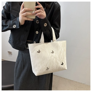 White pleated tote bag with silver metal butterfly charms shown in a lifestyle street shot