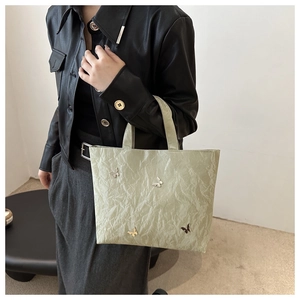Detail of light green pleated tote bag with silver butterfly charms on a model