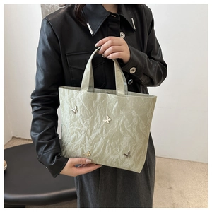 Detail of light green pleated tote bag featuring silver butterfly accents and shiny texture