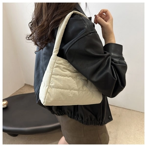 Detail of cream quilted shoulder bag with soft padded texture on female model