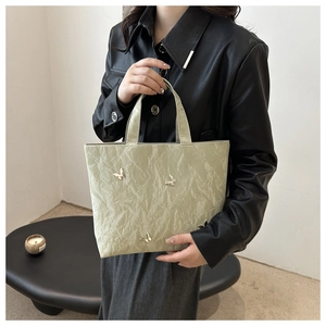 Detail van lichtgroene shopper met geplooide textuur en zilveren vlinderversieringen
