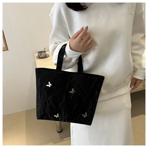 Detail view of black pleated tote bag with silver butterfly metal charms on surface