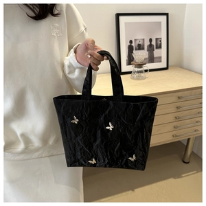 Detailed view of black tote bag featuring crinkled texture and silver butterfly accents