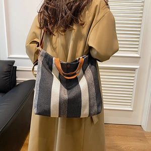 Sac fourre-tout à rayures verticales et anses brunes porté avec un trench-coat chic