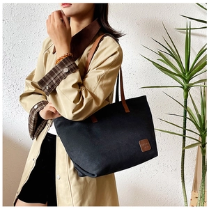 Détail d'un sac cabas en toile noire avec lanières en cuir marron et logo carré