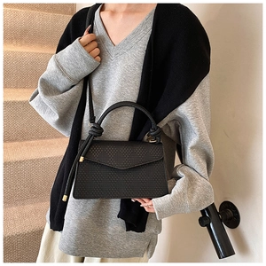 Detail of black woven texture handbag featuring a unique knotted handle and triangle flap