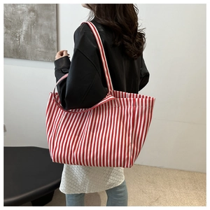 Vue détaillée d'un grand sac cabas en toile à rayures rouges et blanches porté à l'épaule