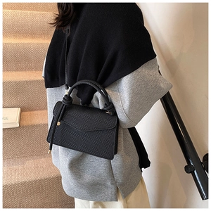 Close-up of black woven texture handbag with knot detail worn crossbody on a staircase