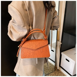 Detailed back view of a burnt orange lace-embossed crossbody bag worn by a model
