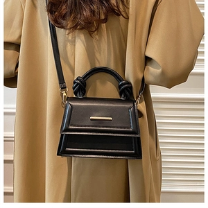 Macro detail of black leather crossbody bag featuring gold buckle and knotted top handle