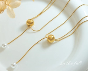 Gros plan d'un collier chaîne serpent dorée avec fermoir réglable et perle pendante