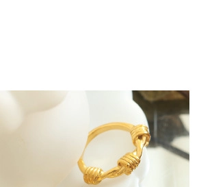 Détail d'une bague en acier titane doré avec un motif de trois nœuds torsadés élégants