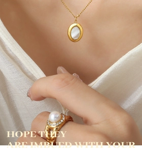 Detalle de collar con colgante de concha y anillo de perla dorada sobre seda blanca