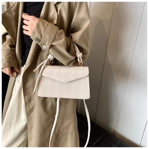 Detail of cream woven handbag featuring geometric texture and white knotted handle