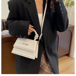 Chic white shoulder bag with knotted handle and gold hardware on model in black blazer