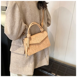 Detail of beige lace-embossed shoulder bag featuring unique knotted handle and gold buckle