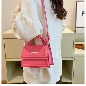 Pink crossbody bag detail featuring a unique knotted handle and gold metal bar buckle