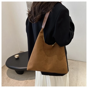 Side view of a brown suede shoulder bag worn by a model in a minimalist setting
