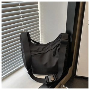 Detail of black nylon tote bag featuring front zipper pocket and adjustable buckle strap