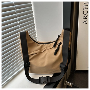 Detail of khaki nylon crossbody bag with adjustable black strap and buckle on windowsill