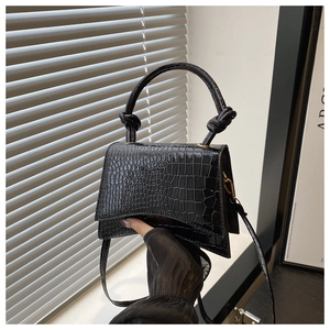 Detail of black crocodile texture bag with knotted top handle and flap closure