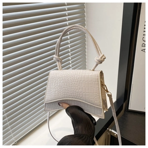 Detailed view of white crocodile pattern handbag with unique side knot handles and strap