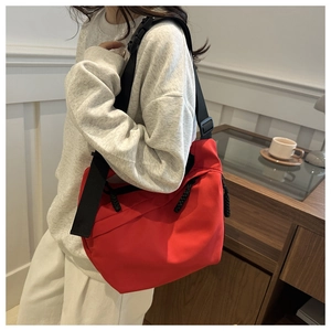 Detailed view of red nylon messenger bag with wide black strap on a male model