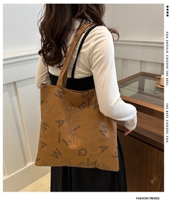 Detail view of large brown tote bag with letter prints worn by model in cozy room