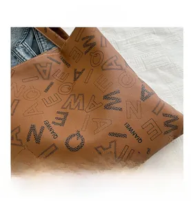Close-up of brown faux leather tote with all-over letter print and lychee grain texture