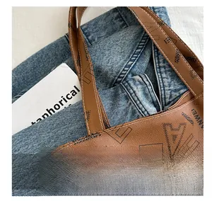Detail of brown faux leather tote bag with black letter print and white stitching accents