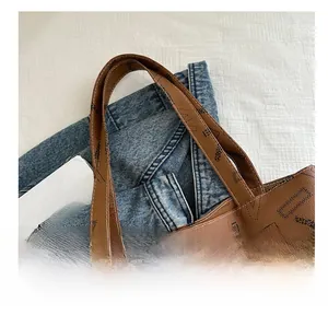 Detail of a brown leather tote bag with letter prints on a denim jacket background