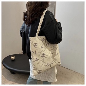 Close-up of large cream tote bag with black letter print worn over a leather jacket