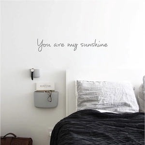 Detail of 'You are my sunshine' wall sticker above minimalist Nordic bedding decor