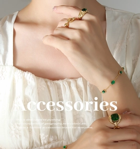 Detail view of emerald zircon gold-plated bracelet and rings on model with white textures