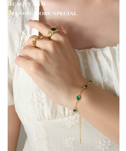 Detailed shot of 18K gold-plated bracelet and rings with emerald green zircon stones
