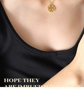 Macro detail of gold-plated double happiness pendant necklace on a black background