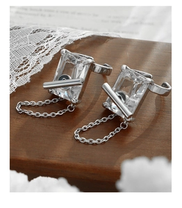 Detailed shot of silver-toned zircon earrings with chain tassels on dark wood background