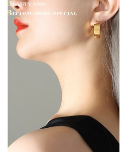 Close-up of a model wearing polished gold rectangular hoop earrings in a minimalist style