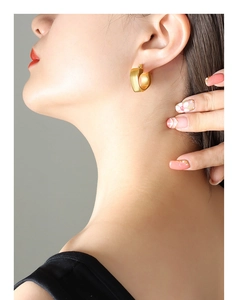 Close-up of matte gold hollow heart hoop earring worn by a model in a minimal setting