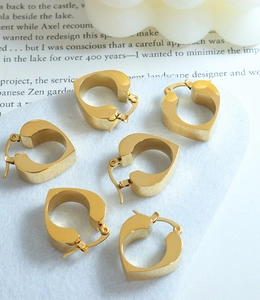 Detailed view of three pairs of hollow heart-shaped gold hoop earrings on white texture