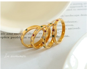 Detailed view of four gold-plated rings with colorful red, green and white zircon inlays