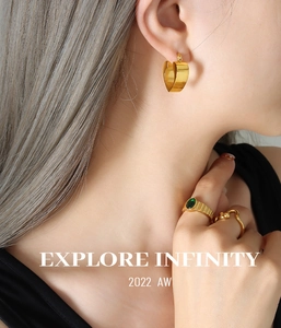 Close-up of golden hollow heart earrings with green gemstone ring and wavy band on model