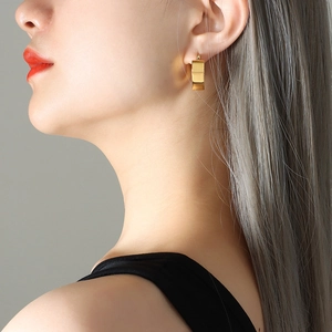 Polished gold geometric wide-band earrings with faceted design shown on a female model