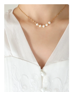 Gros plan d'un collier en chaîne dorée avec cinq perles blanches dégradées sur mannequin