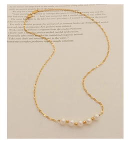 Détail du collier en chaîne dorée avec cinq perles blanches et billes d'or sur livre