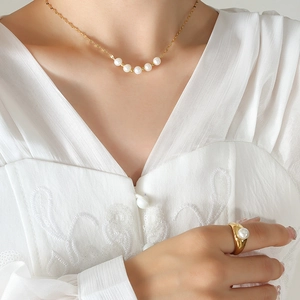 Collier doré élégant avec cinq perles et bague assortie sur une blouse en dentelle