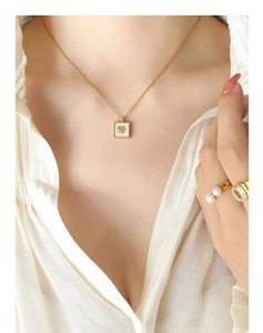 Primo piano della collana con camelia dorata e anelli su modella con luce soffusa