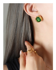 Gros plan sur une boucle d'oreille émeraude et une bague dorée portée par un mannequin